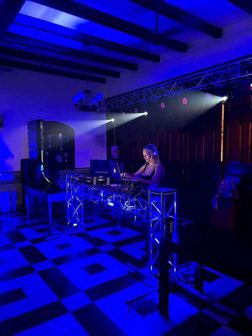 DJ tocando en cabina de truss iluminada en un salón, con luces de Cooksound